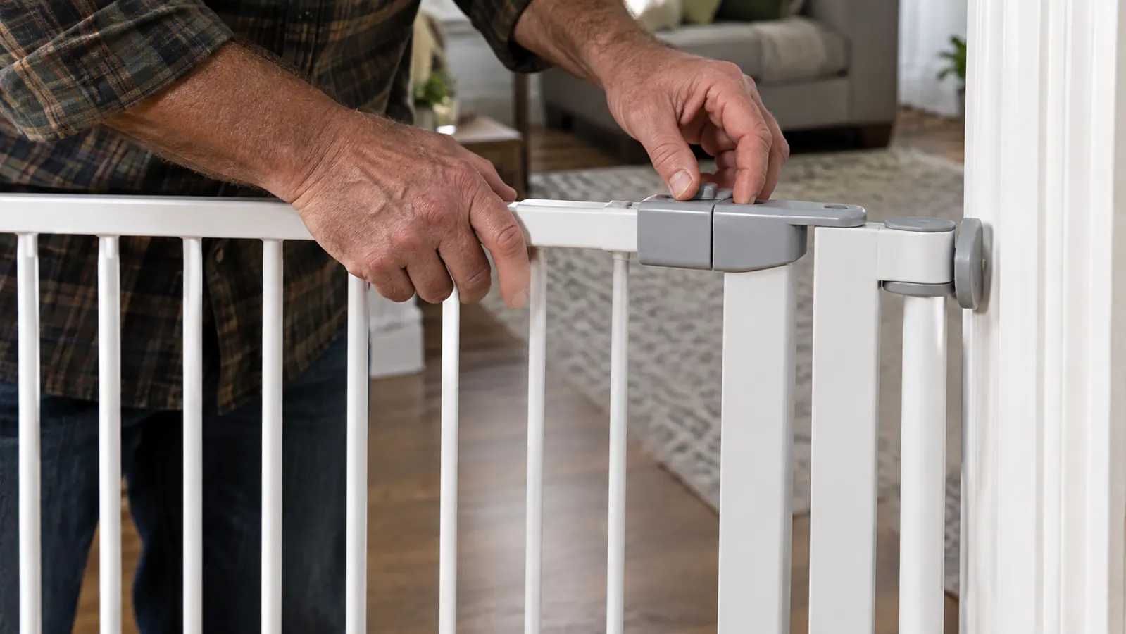 A person's hands adjusting the top latch of a freestanding pet gate between two rooms